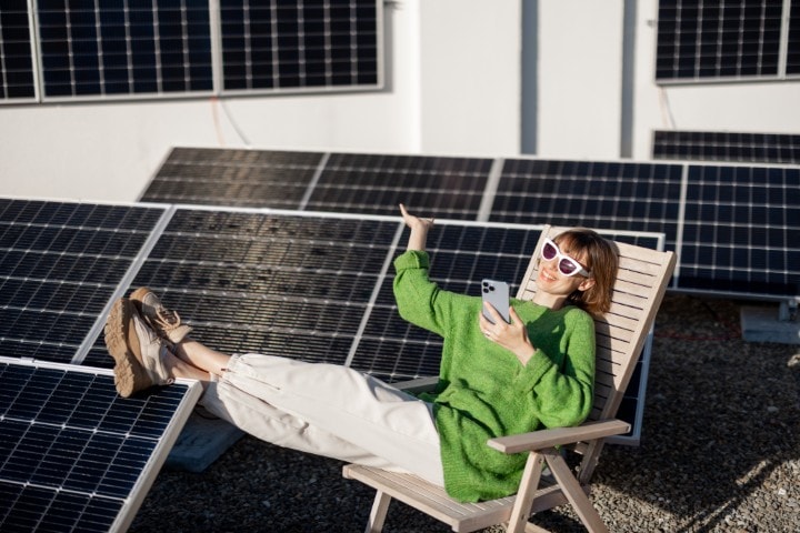 Woman sat in front o solar panels checking her phone